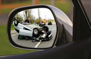 A traffic accident with a white car flipped on its roof as seen through a side mirror on the Archangel Law Group website Traffic Court page